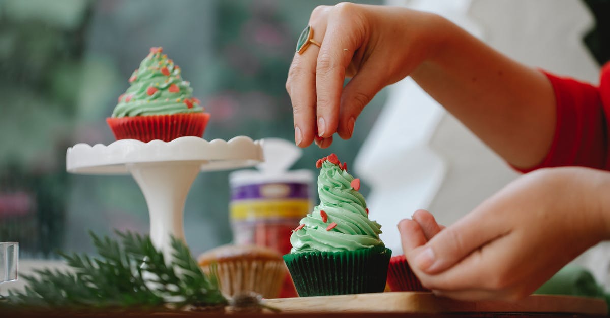 How to put stuff inside baked sandwich and bread? - Unrecognizable female sprinkling topping on green frosting of cupcake while standing near windowsill with wooden board and coniferous branch on blurred background