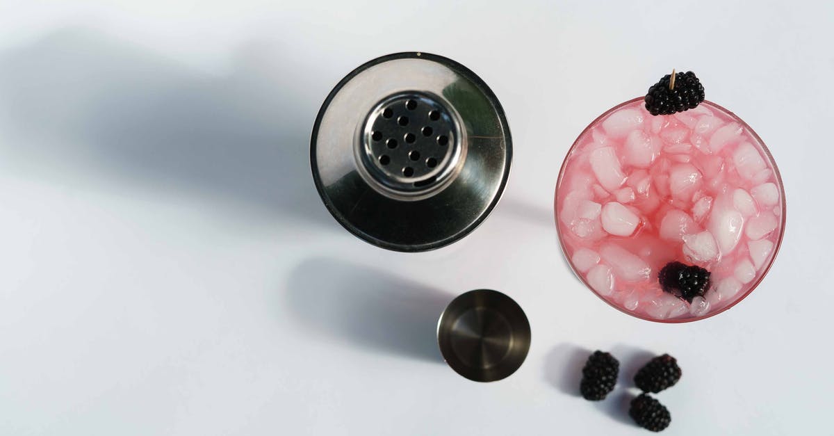 How to refresh a frozen bagel - Top view of glass of cold blackberry margarita with berries and ice cubes near stainless shaker on white background