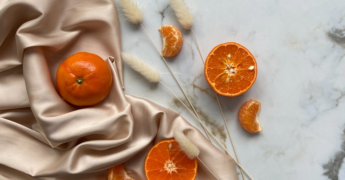 How to remove a smokey/ charcoal taste from food? - Top view of fresh ripe slices of tangerine and oranges placed on crumpled fabric on marble surface with dried branches