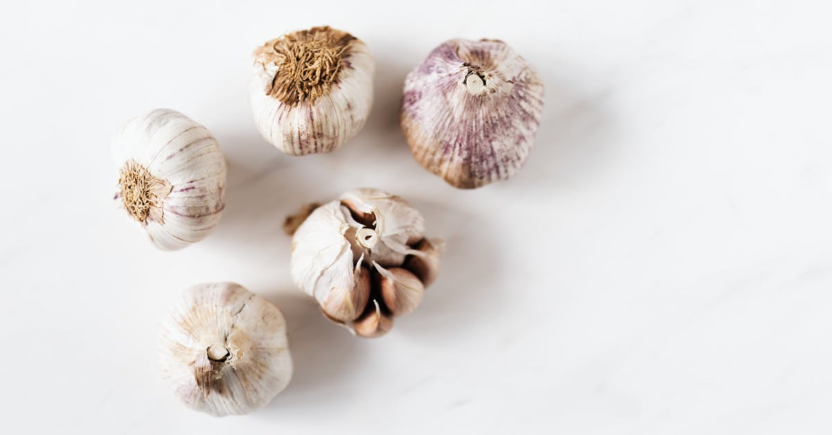 How to remove garlic smell from refrigerator/ice maker - Top view of unpeeled raw yellow onion in white bowl and unpeeled raw aromatic garlic in light green bowl placed on marble table