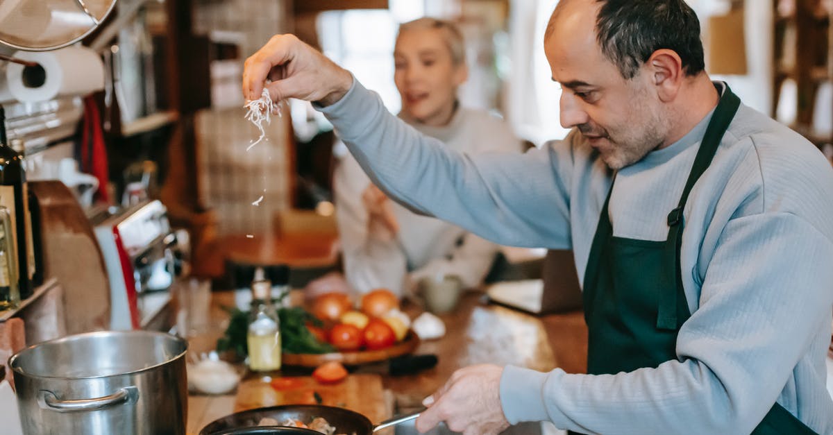 How to season iron cookware on gas stove? - Focused male in apron adding ingredient into frying pan heating on gas stove while cooking meal for woman