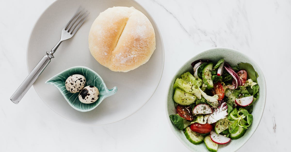 How to serve fresh bao buns - From above of healthy diet salad in bowl and plate with quail eggs fork and bun placed on white marble table