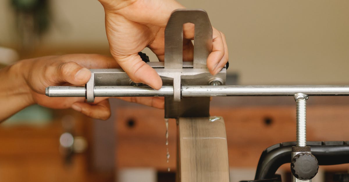 How to sharpen knife with chunk missing? - Side view of unrecognizable craftsman sitting at sharpening machine with metal stick while grinding knife in professional studio on blurred background