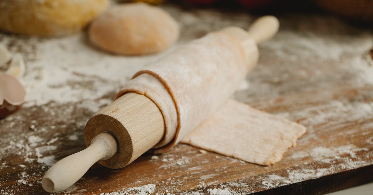 How to smooth a wooden rolling pin - Wooden rolling pin with soft thin dough on table with spilled flour in kitchen