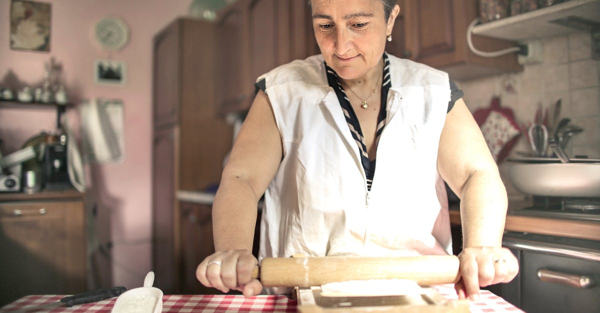 How to smooth a wooden rolling pin - Aged female baker rolling gough with pin while cooking in cozy kitchen at home