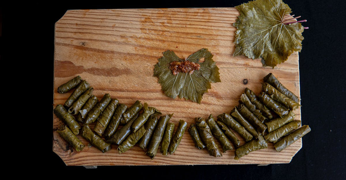 How to soften diced meat that was has had too much of its juices leave from being cooked too long? - Top view of sarma rolls near vine leaves with meat filling on wooden table on black background