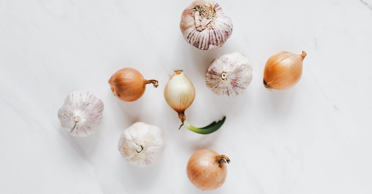 How to suppress bad breath after eating garlic or onion - Top view composition of raw unpeeled ripe yellow onions and fresh whole aromatic garlic bulbs placed on white marble background