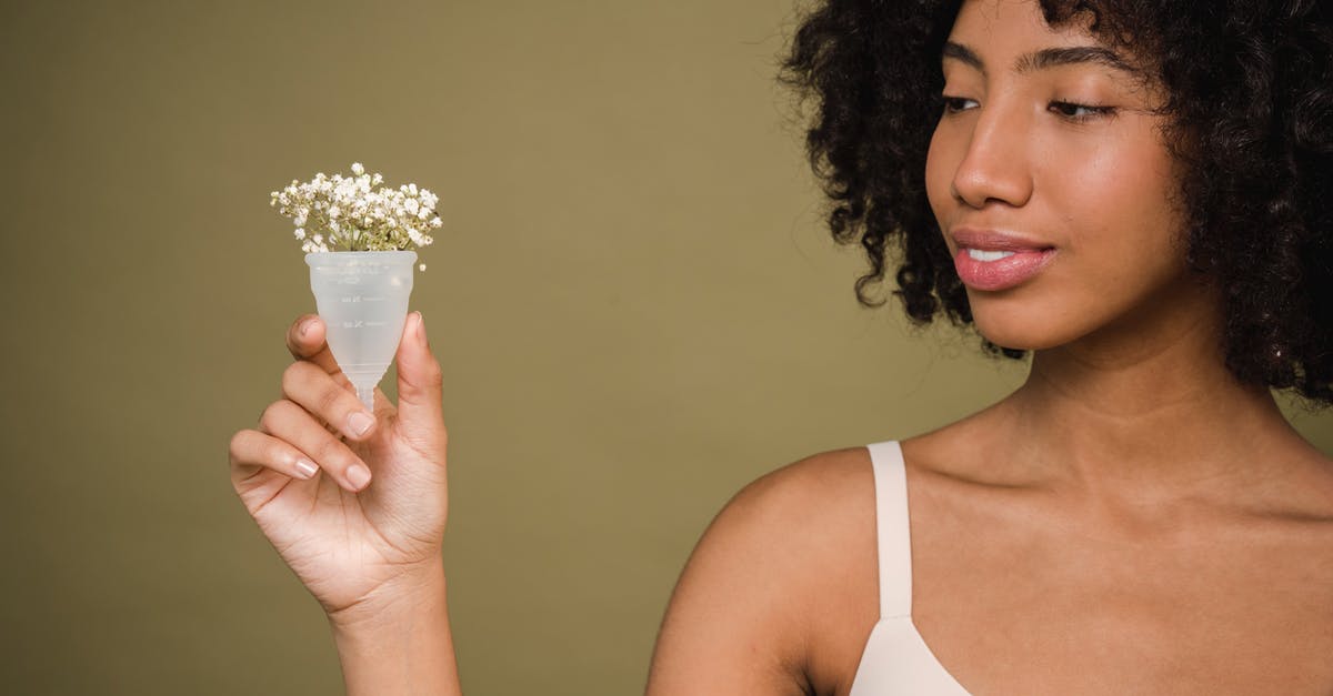 How to take care of Silicone cookware - Happy young African American female model with curly hair in bra smiling and showing menstrual cup with gentle flowers against beige background