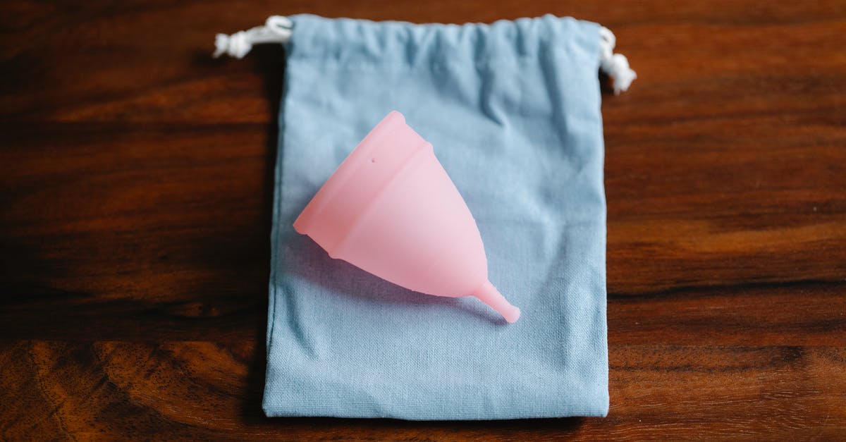 How to take care of Silicone cookware - Top view of pink menstrual cup for feminine hygienic procedure on cloth bag placed on wooden table in light room