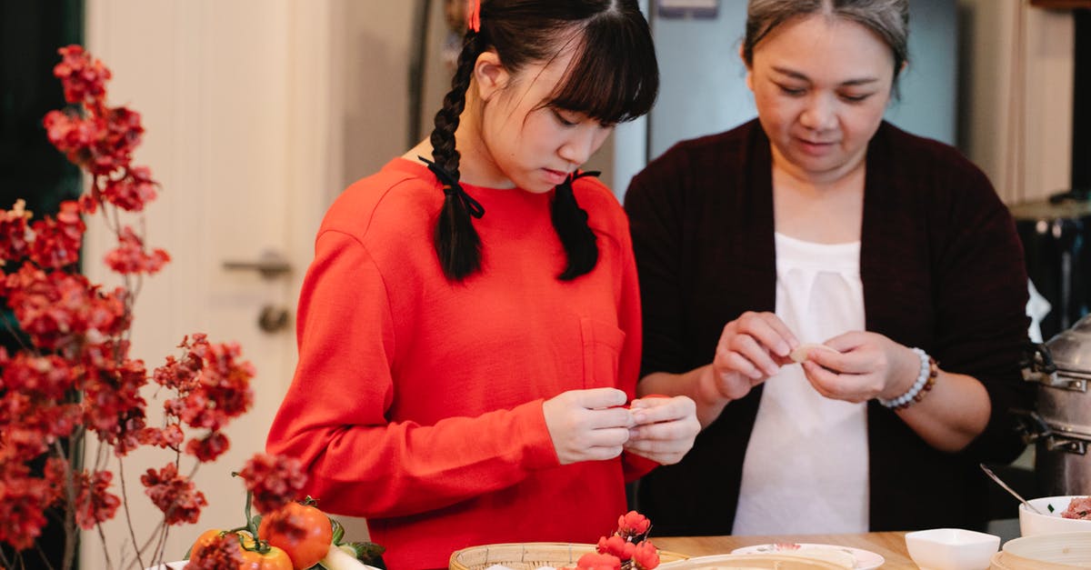 How to tell if a vegetable steamer contains titanium - Ethnic grandma with teen preparing traditional oriental dish at table with fresh vegetables and steamer in house