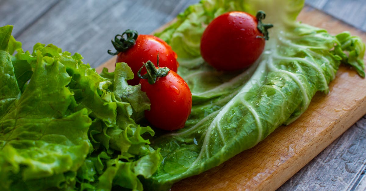 How to wash lettuce - From above of assorted varieties of lettuce leaves placed on wet wooden cutting board with ripe appetizing tomatoes in kitchen in daylight