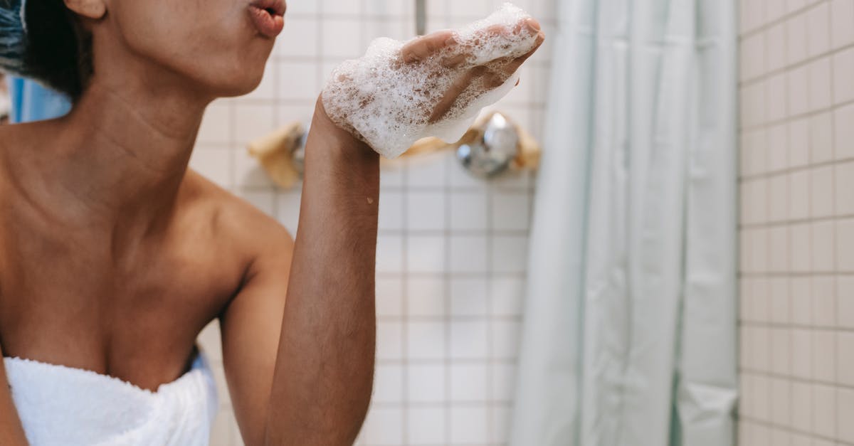 How to wash soft fruit? - Side view of crop anonymous African American female in towel blowing off foam from hand in bathroom