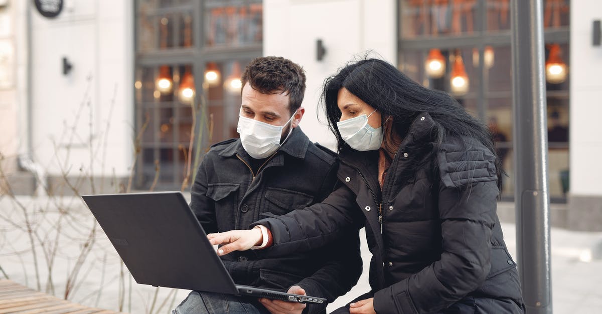 How warm must dough be in order to rise? - Focused colleagues wearing warm outerwear with protective masks on faces surfing laptop during remote teamwork sitting on wooden bench against urban building