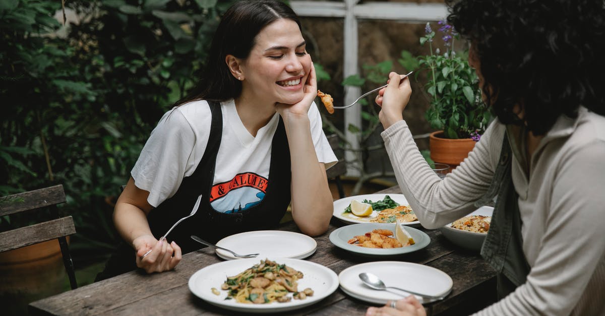 I cannot understand how to properly fry seafood - Female giving food on fork to cheerful friend while having lunch in outdoor terrace