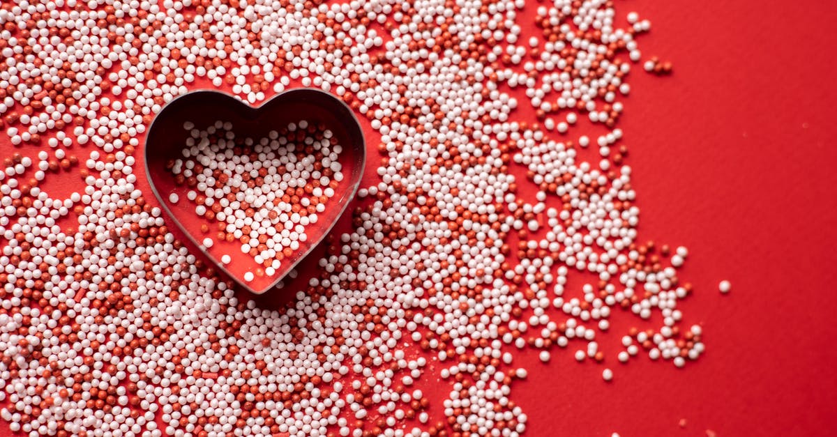 I love palm sugar, when can I bake with it - Top view of heart shaped form for baking among sweet sugar sprinkles scattered on red background as symbol of Saint Valentines Day