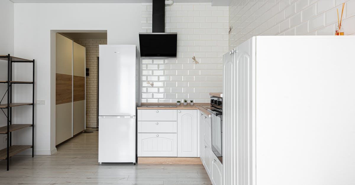 Ice-cream-on-a-stick in refrigerator temperature - Contemporary kitchen with refrigerator and hood against decorative white brick wall in house with empty shelves on parquet