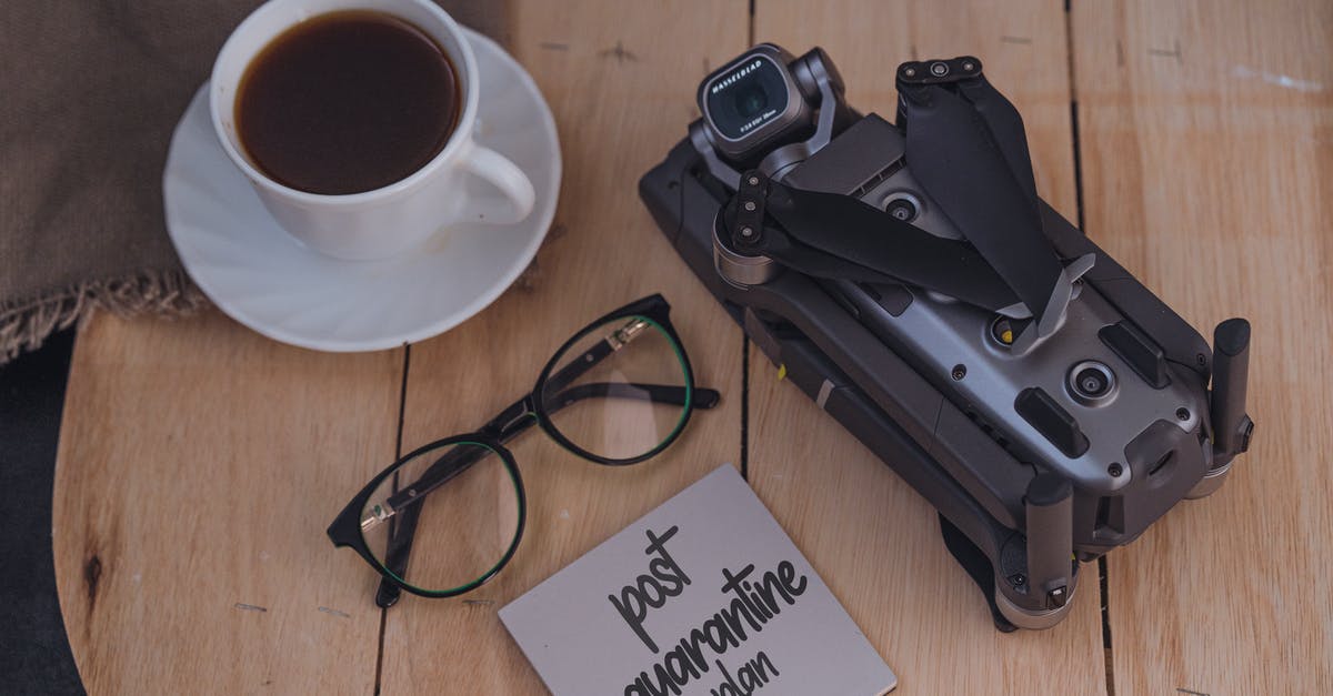 Impossible to manage sticky dough - From above of coffee cup and eyeglasses placed on wooden table near folded drone and sticky note with post quarantine plan inscription