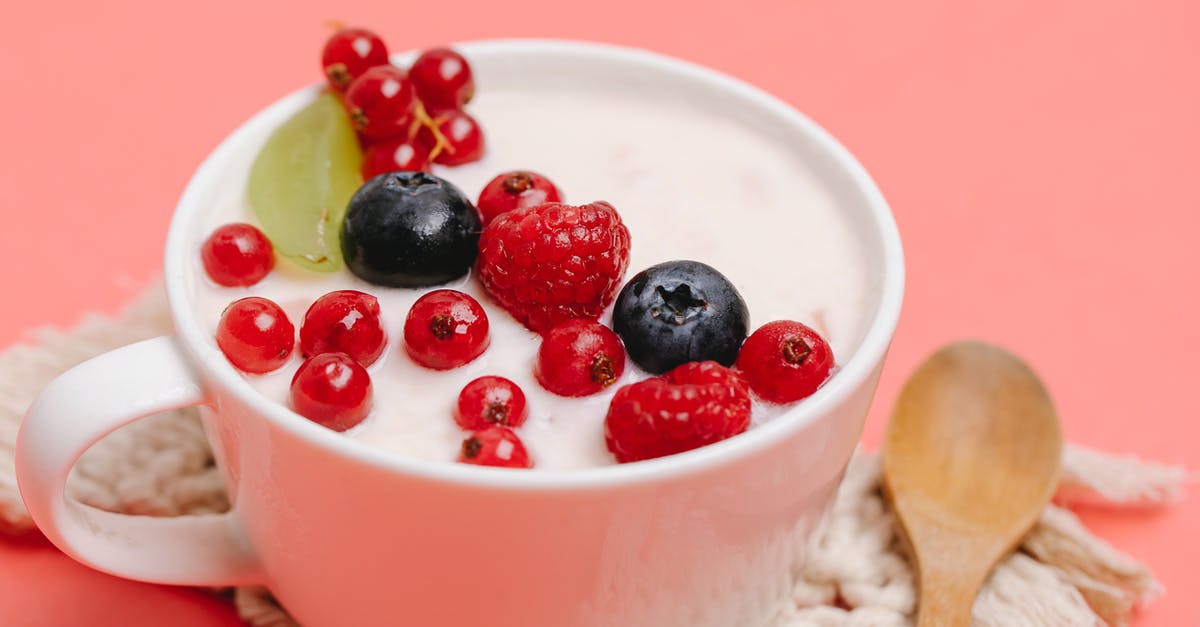 In a recipe, yogurt toughens potatoes but whipping cream does not - From above of delicious homemade yogurt in white ceramic mug decorated with assorted berries and served on pink table with wooden spoon