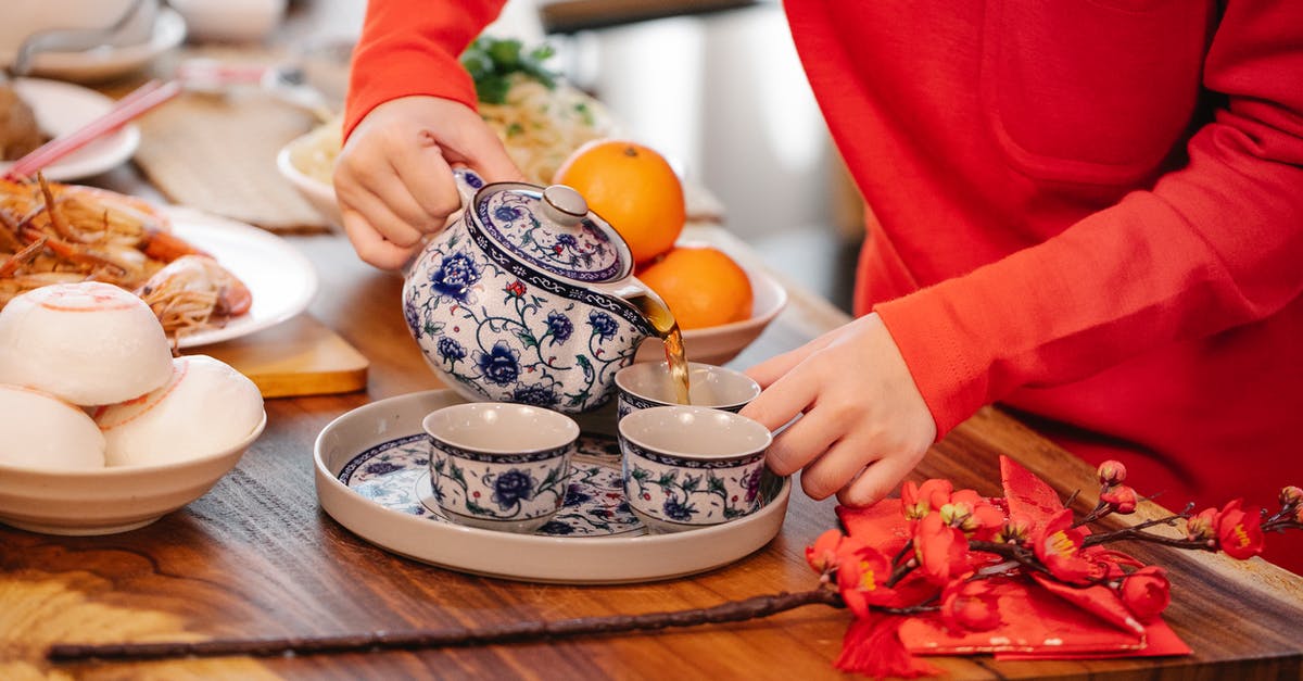 Infusing orange into tea while avoiding bitterness - Crop unrecognizable female pouring hot beverage from ornamental teapot into cup at table with oriental dishes in house