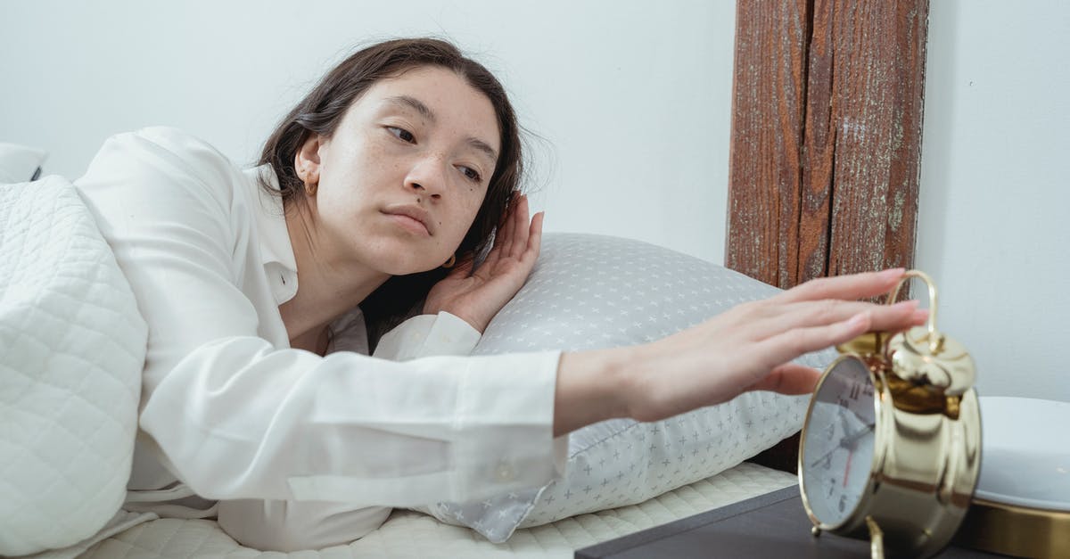 Inside of the cookies turn up soft, almost uncooked? - Sleepy young brunette female in white sleepwear resting in comfortable bed and waking up with alarm clock at home in morning time