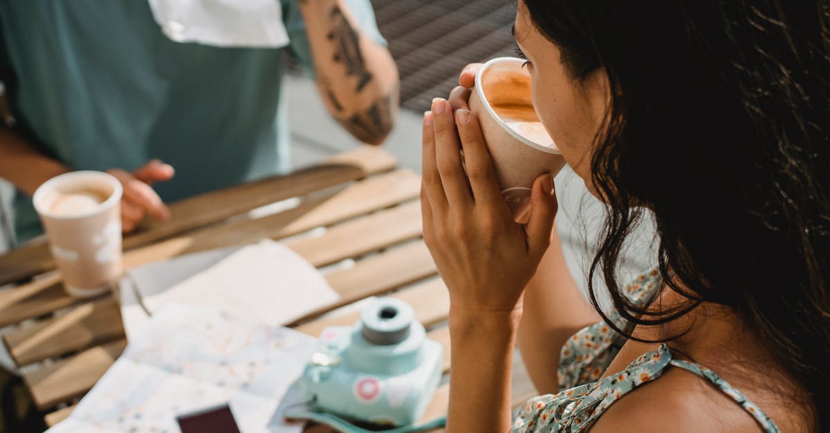 Instant coffee with only milk? - From above of crop anonymous couple drinking coffee while sitting at table with map and instant photo camera during vacation together