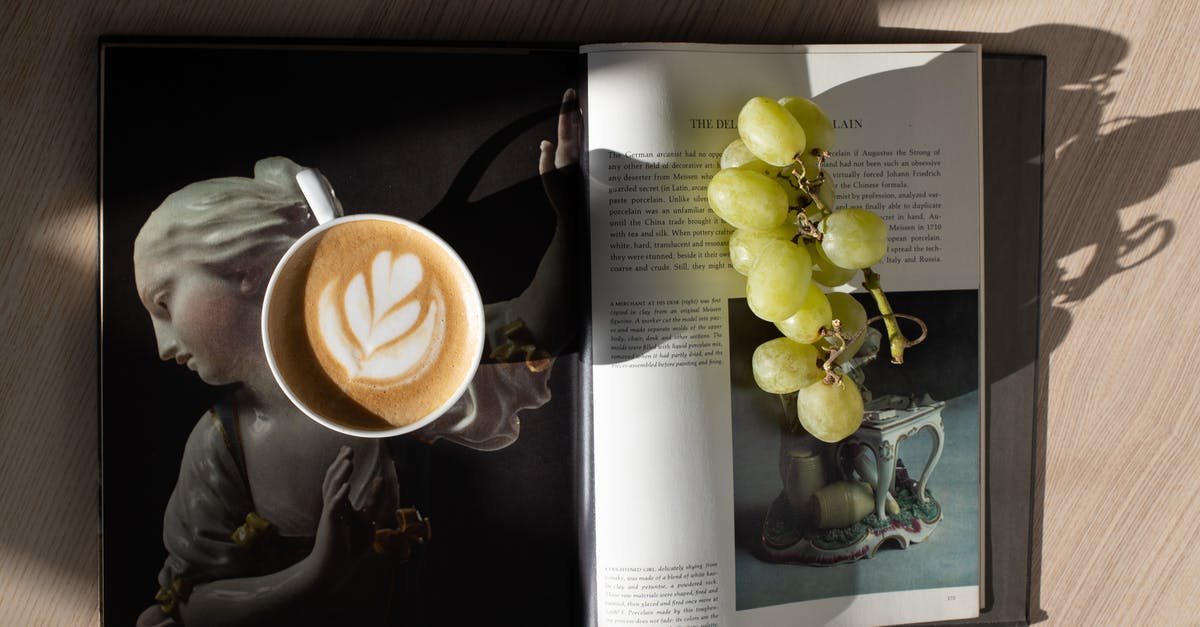 Interesting use for Okra as the main ingredient in a dish? - Top view of cup of fresh brewed cappuccino with latte art and bunch of healthy green grapes placed on opened magazine on wooden table