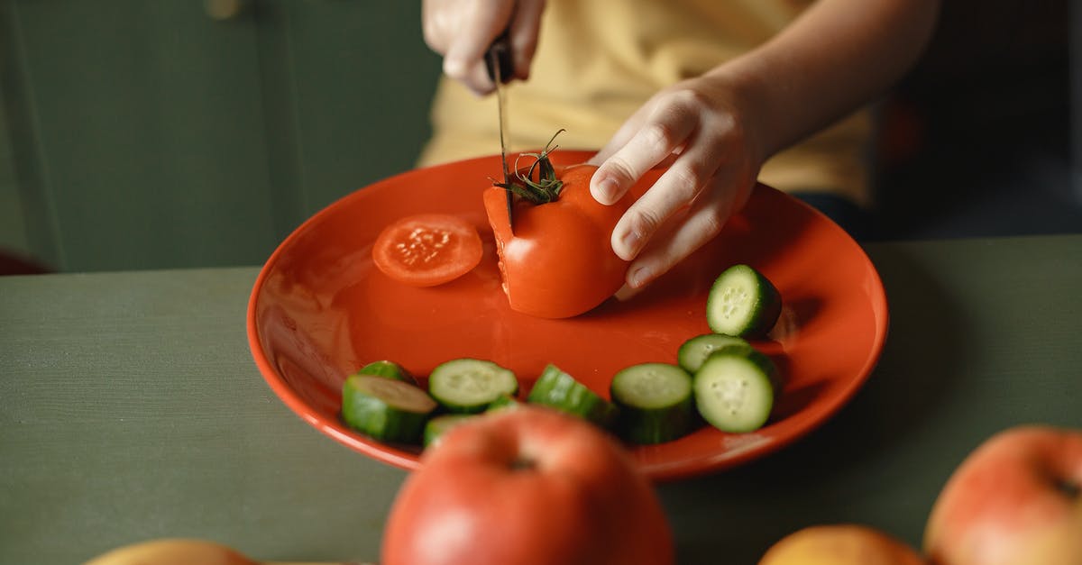 Is a partially translucent banana safe to cook with? - Unrecognizable kid cutting fresh tomato with knife on red ceramic dish with cucumber slices placed on table with assorted fruits while preparing healthy salad