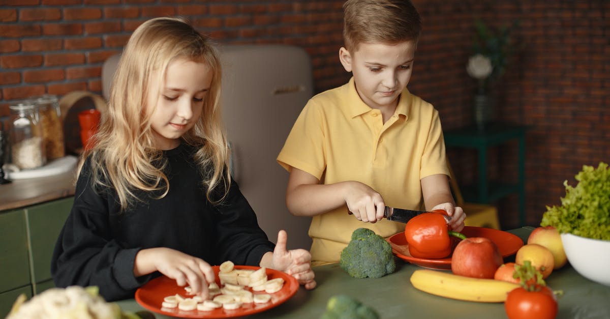 Is a partially translucent banana safe to cook with? - Focused little girl and boy cutting various vegetables and fruits while sitting at table and cooking in loft kitchen with brick wall