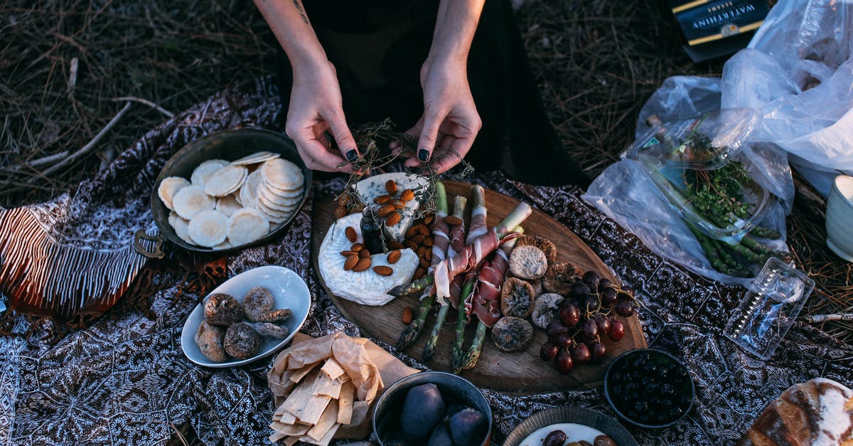 Is eating olive pits a problem? - From above crop anonymous female serving yummy food including asparagus with bacon potatoes and grapes on wooden board placed on plaid during picnic in nature