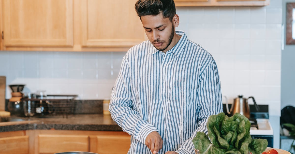 Is having an extending blade near the knife handle a serious risk when cutting food? - Bearded ethnic male in striped shirt cutting fresh tomato with knife against spinach leaves on table at home