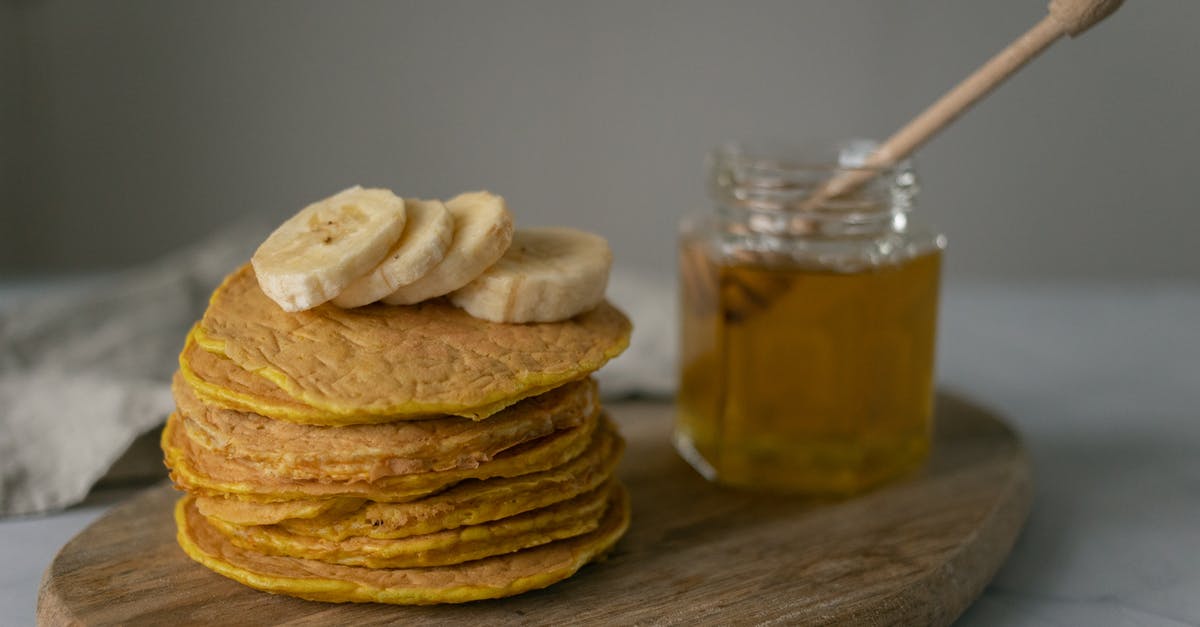 Is honey considered vegan? - Tasty homemade pancakes with sliced bananas near jar with honey and wooden spoon on cutting board on table