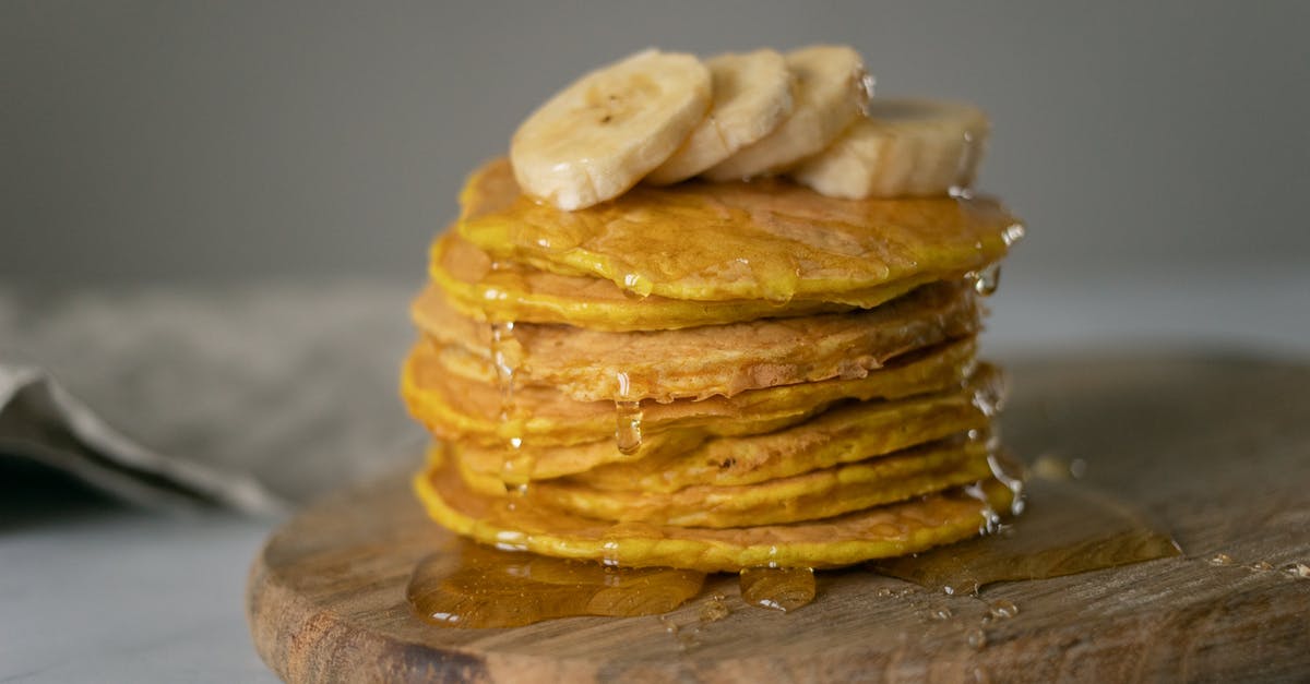 Is honey considered vegan? - Delicious homemade pancakes covered with honey with sliced bananas placed on wooden chopping board on table in light place