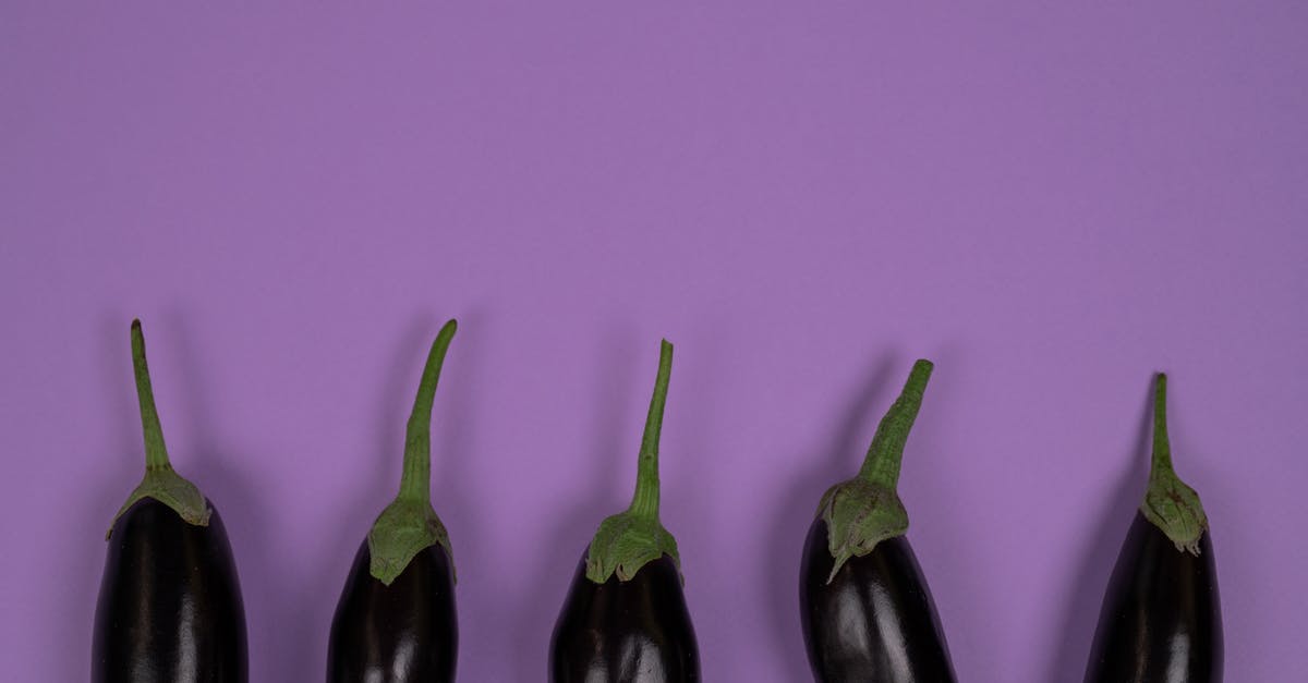 Is it necessary to peel aubergine? - Top view of raw aubergines with smooth peel and stalks on calyces on violet background