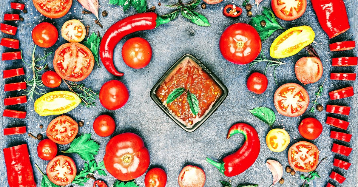 Is it ok to include garlic when I can hot peppers? - Top view of composition of colorful chili pepper and assorted tomato slices near fresh cilantro and parsley leaves with rosemary and thyme sprigs with bowl of savory sauce in center