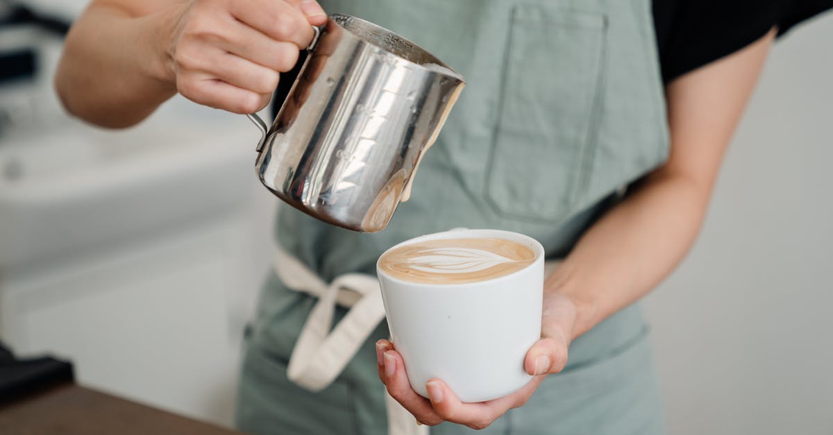 Is it ok to refrigerate almond milk after I add honey to it? - Crop bartender in apron preparing aromatic cappuccino in cup while pouring foam of milk into ceramic cup in coffeehouse