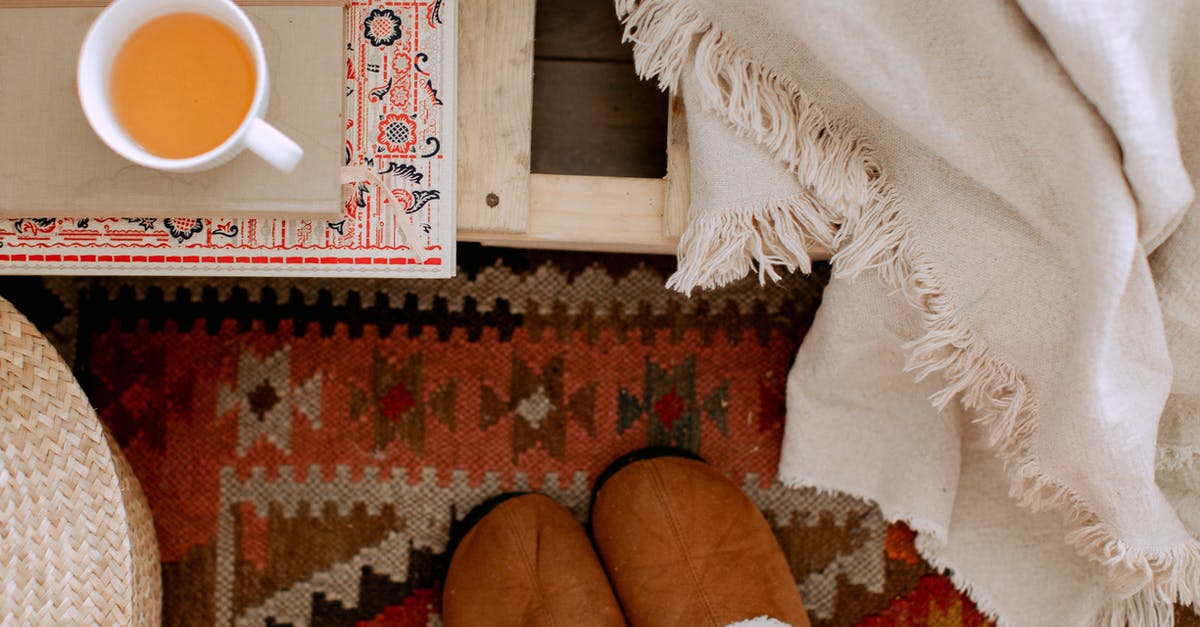 Is it possible to brew good tea on a mountain? - From above of cozy bedroom interior with white plaid, brown warm slippers on carpet, wicker basket and cup of tea on tray