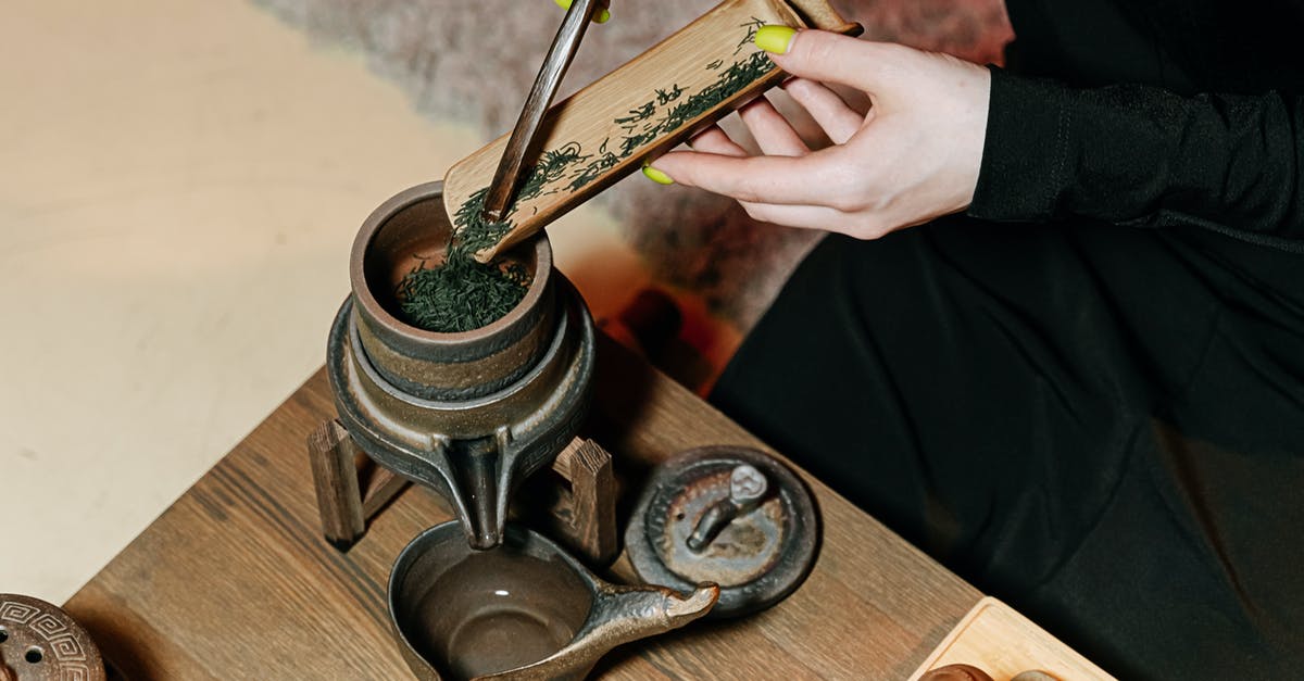 Is it recommended to rinse the teapot with boiling water before putting the tea leaves in? - A Person Putting Green Tea Leaves into a Bowl