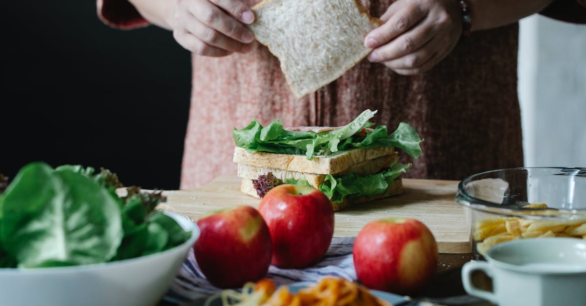 Is it safe to eat an apple cooked inside poultry? - Unrecognizable female cook putting slice of bread on lettuce while standing at table and making sandwich in kitchen during breakfast time