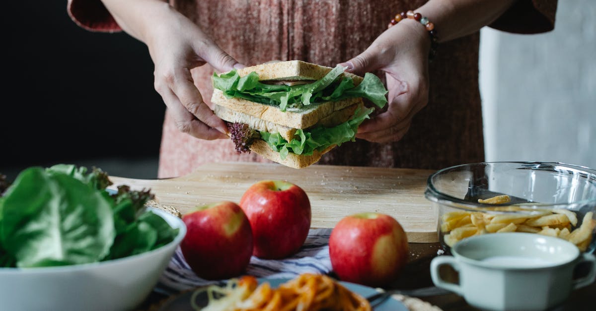 Is it safe to eat an apple cooked inside poultry? - Unrecognizable female standing at table with apples and cutting board with sandwich with lettuce in hands in kitchen on breakfast time