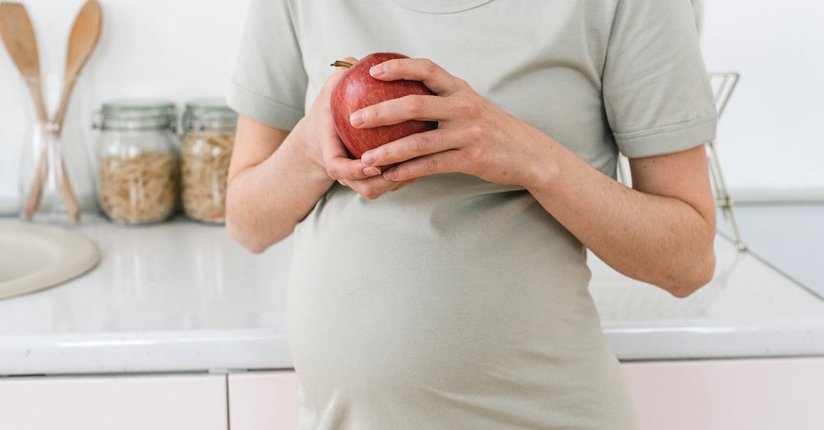 Is it safe to eat an apple cooked inside poultry? - Unrecognizable pregnant female with ripe red apple for healthy diet in hands standing near counter in light kitchen at home