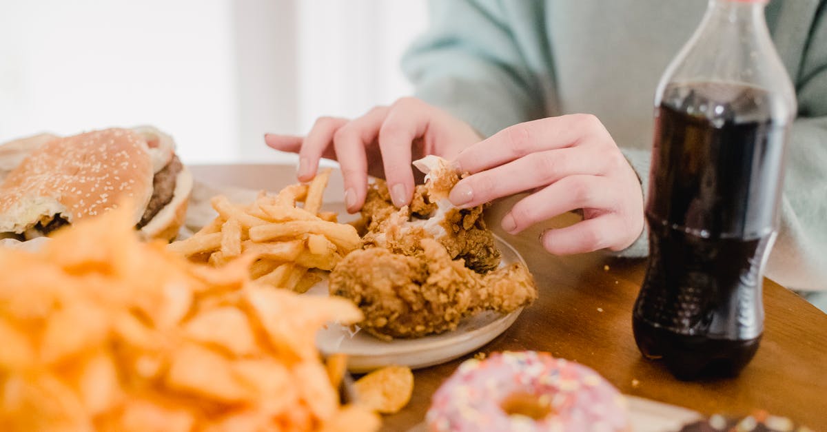 Is it safe to eat chicken that is still frozen? - Woman eating fried chicken and fries at table with lemonade Is it safe to eat chicken that is still frozen? - Woman eating fried chicken and fries at table with lemonade