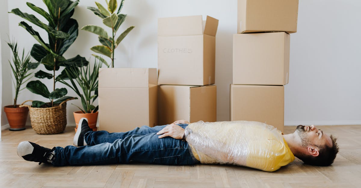 Is it safe to use plastic wrap in boiling water? - Full body side view unemotional male wearing casual outfit lying on floor with upper body tied up with tape and tired after packing belongings into carton boxes