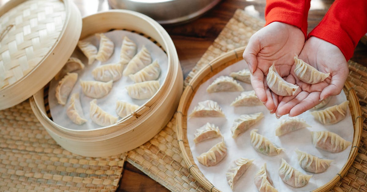 Is it safe to use staples or paper clips to seal parchment paper when cooking fish en papillote? - High angle of crop anonymous female showing raw dumplings over table with bamboo steamer in house