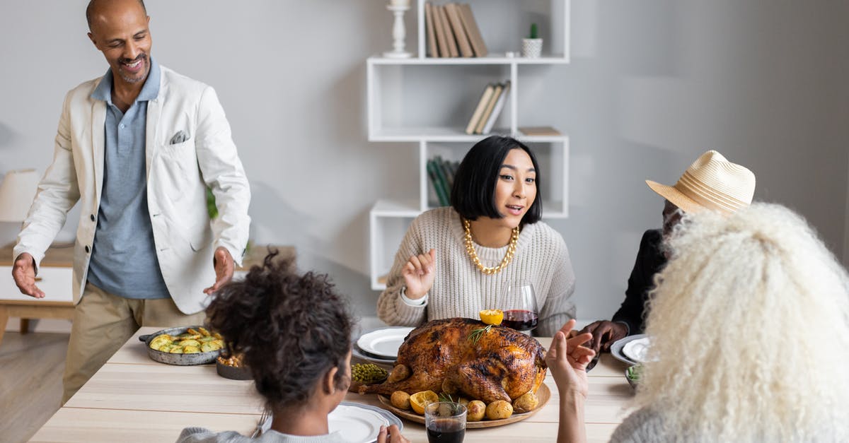 Is the oily liquid from roasting a turkey worth keeping? - From above of glad diverse people speaking with each other while sitting at wooden table with food and having Thanksgiving dinner