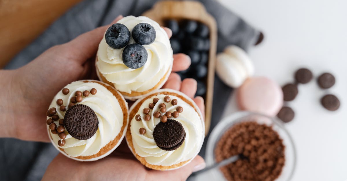 Is there a basic, universal recipe for cupcakes? - Top view of crop anonymous person showing delicious cupcakes with blueberries and chocolate sweets against blurred background of various dessert