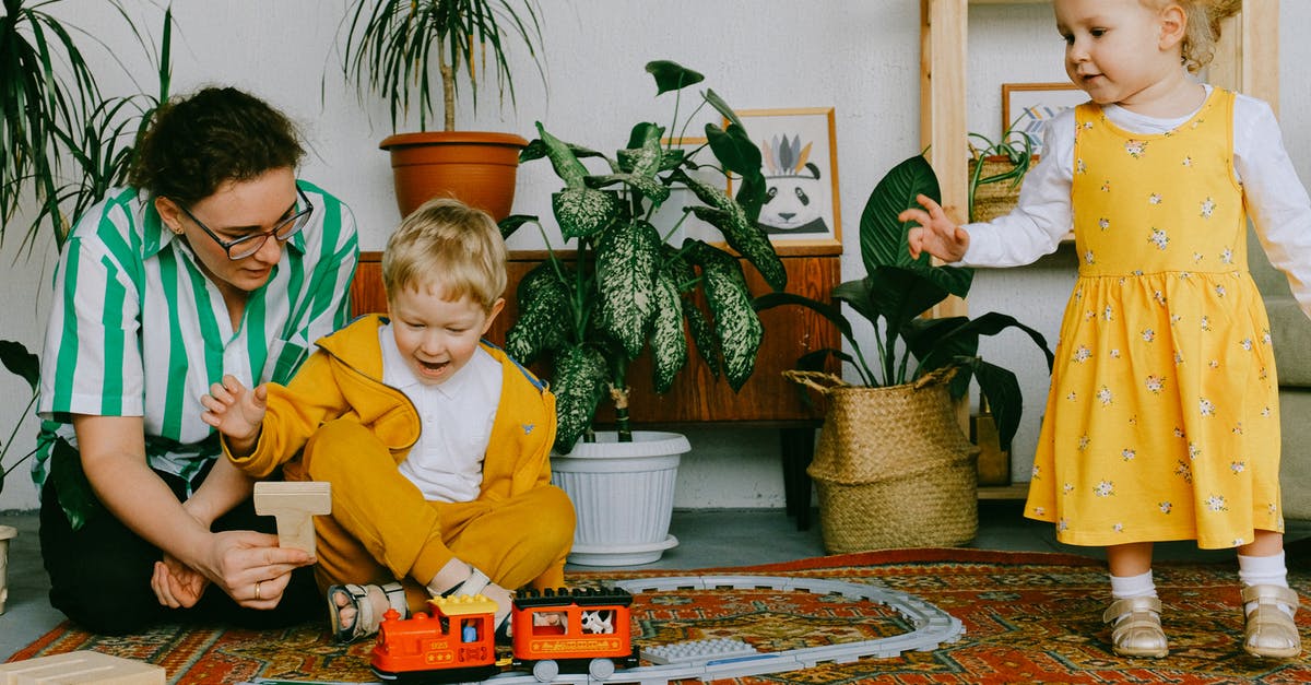 Is there a reason to have a plastic bowl? - Mom and adorable little brother and sister in casual wear gathering in cozy living room during weekend and having fun together while playing with plastic railway