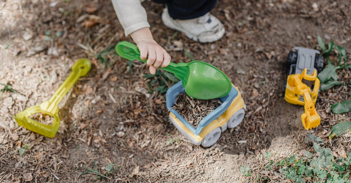 Is there a reason to have a plastic bowl? - Unrecognizable little child playing with plastic toy car and shovel in calm sunny yard