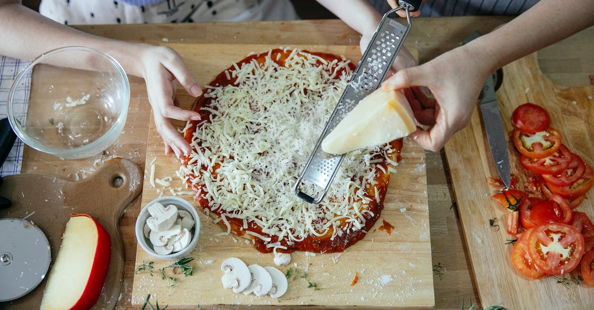 Is there a reason to not grate cheese ahead of time? - Overhead crop women grating hard cheese together while cooking pizza on wooden table with various ingredients and utensil in kitchen