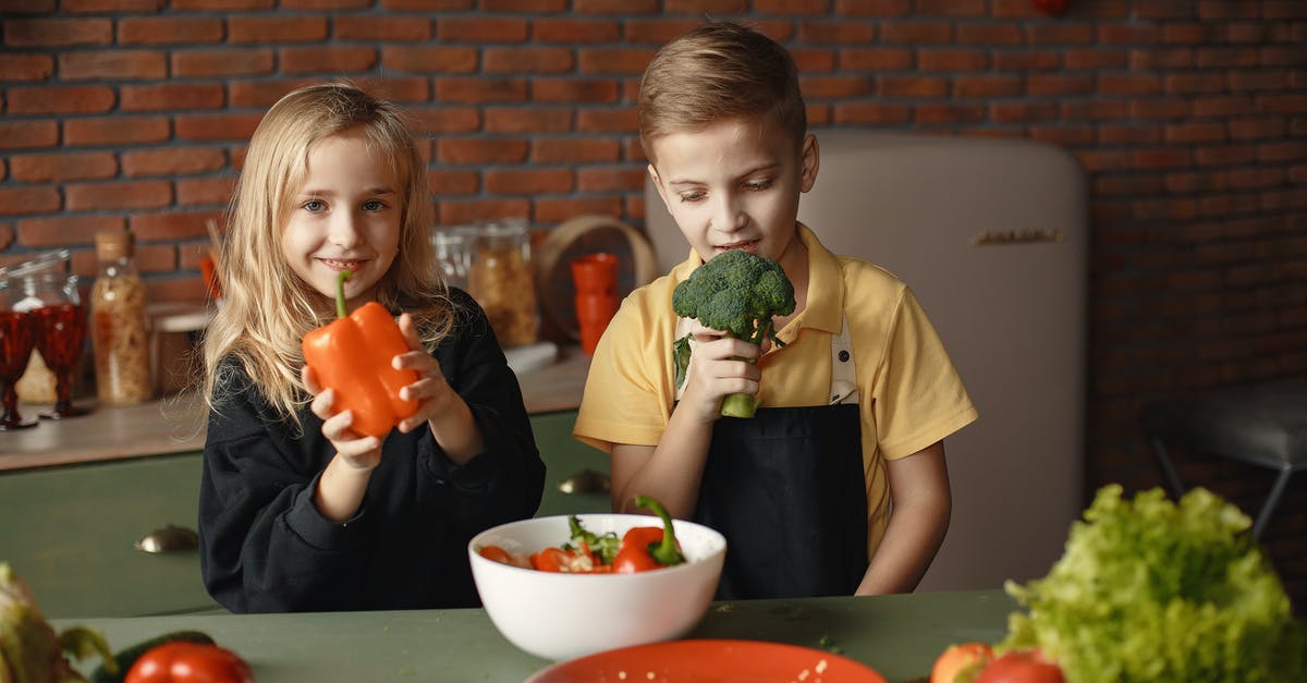 Is there a way to lessen the unpleasant smell of steamed broccoli? - Cute girl and boy with fresh pepper and broccoli in hands standing near desk with assorted vegetables and salad bowl during vegetarian meal preparation