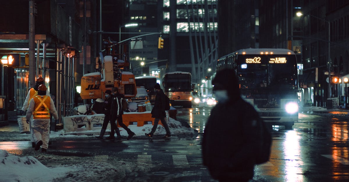 Is there a way to safely can pesto sauce? - People in medical masks strolling on crosswalk near roadway with glowing buses on dark street during winter evening in city